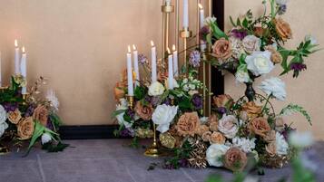 En række høje, hvide lys med gyldne fodstykker, omgivet af blomsterarrangementer.