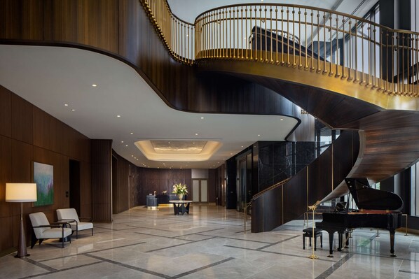 Un vestíbulo espacioso con un piano de cola, una escalera curva y una mesa de recepción.
