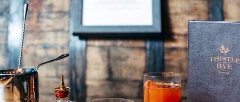 Un decantador de whisky, un vaso de whisky y una botella de whisky sobre una mesa de madera, con un cuadro en el fondo.