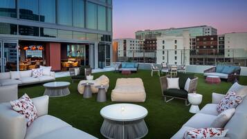 A rooftop lounge with outdoor seating, a bar, and a view of the cityscape.