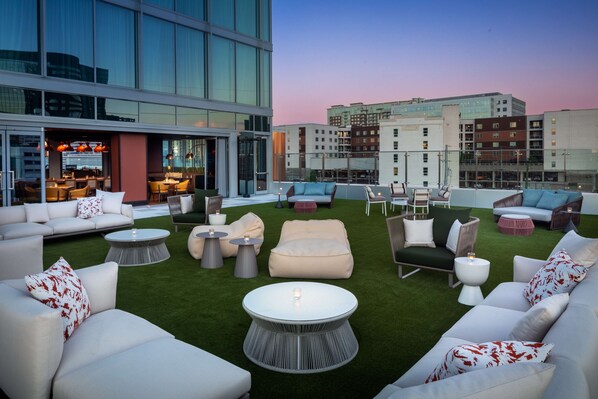 A rooftop lounge with outdoor seating, a bar, and a view of the cityscape. - Conrad Nashville (Nashville)