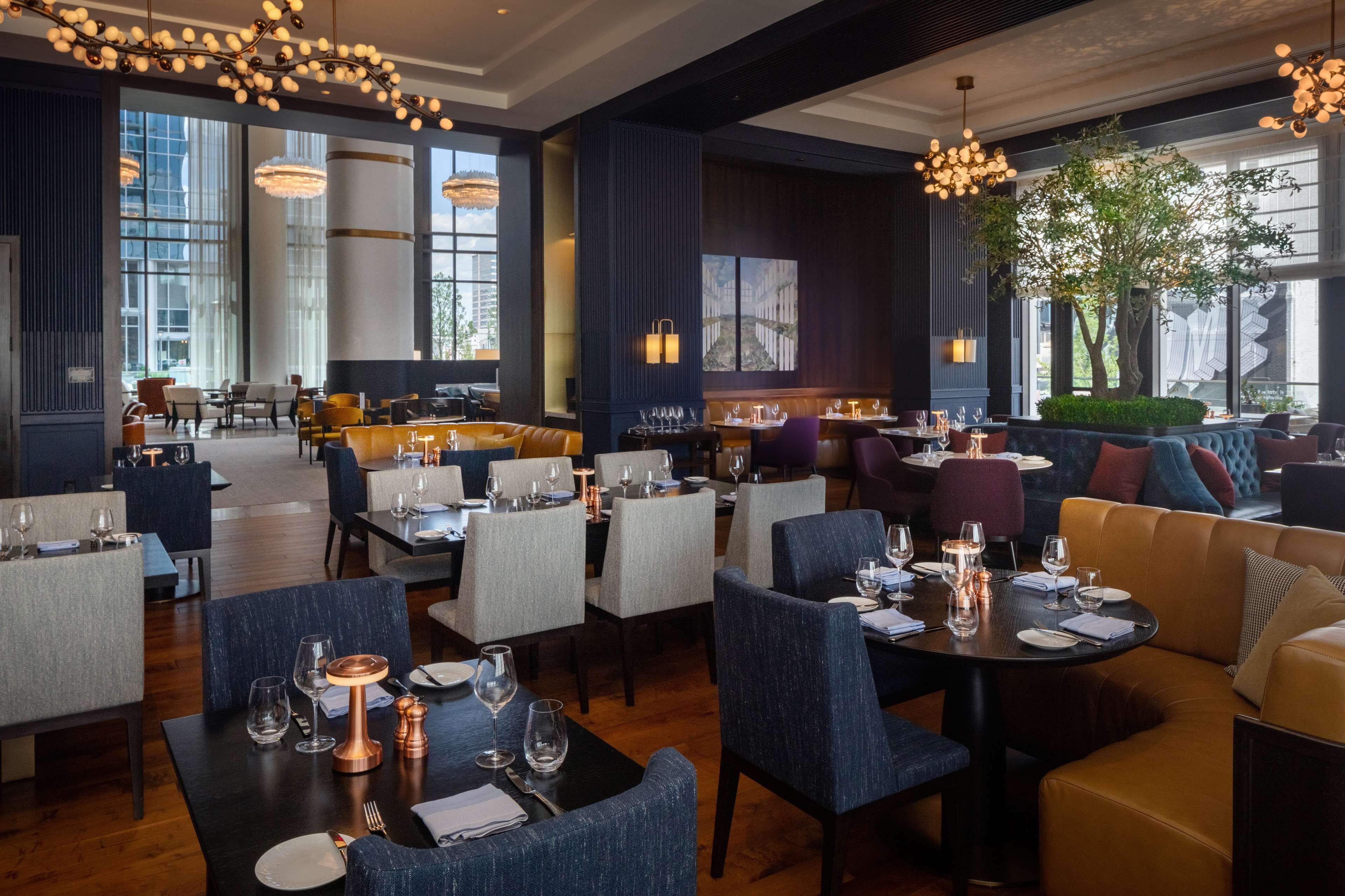 A modern restaurant with high ceilings, large windows, and a mix of seating options including tables and sofas.