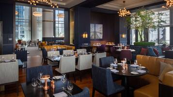 A modern restaurant with high ceilings, large windows, and a mix of seating options including tables and sofas.