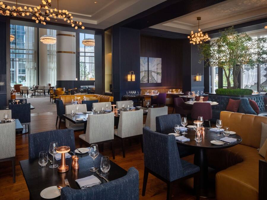 A modern restaurant with high ceilings, large windows, and a mix of seating options including tables and sofas.