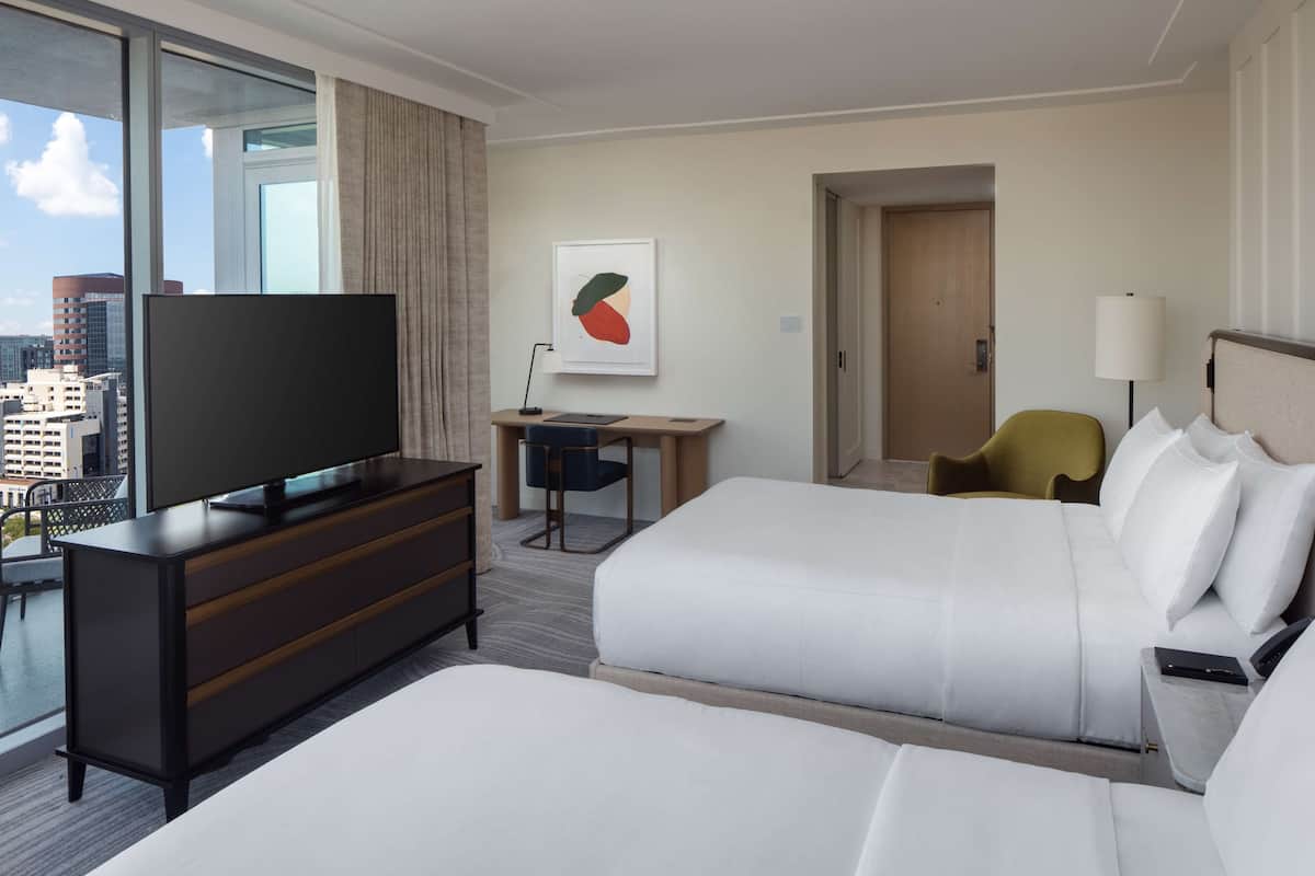 A hotel room with a large bed, a TV on a dresser, a desk with a chair, and a city view.