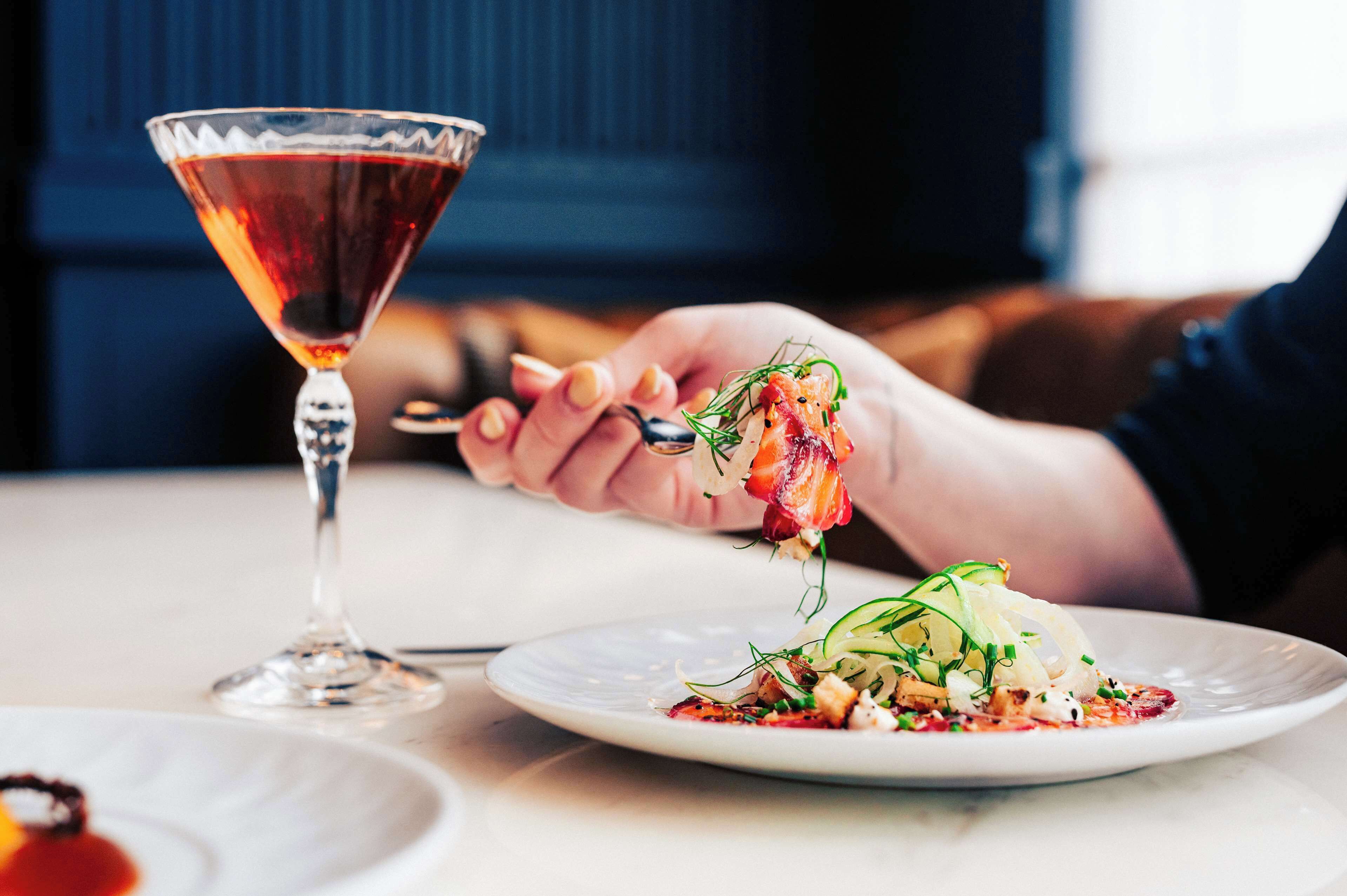 Une personne est assise à une table, devant un verre de vin rouge et une assiette de nourriture.