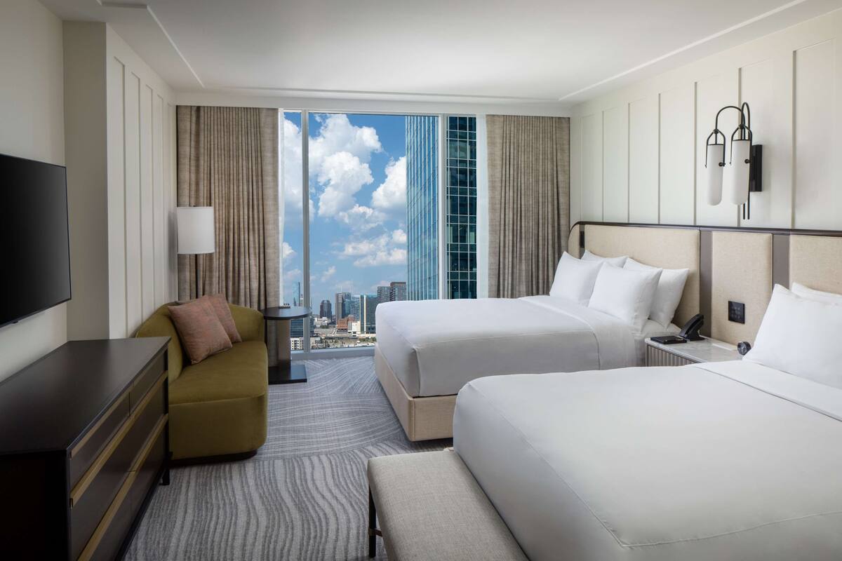 A hotel room with two beds, a sofa, a TV, and a city view.
