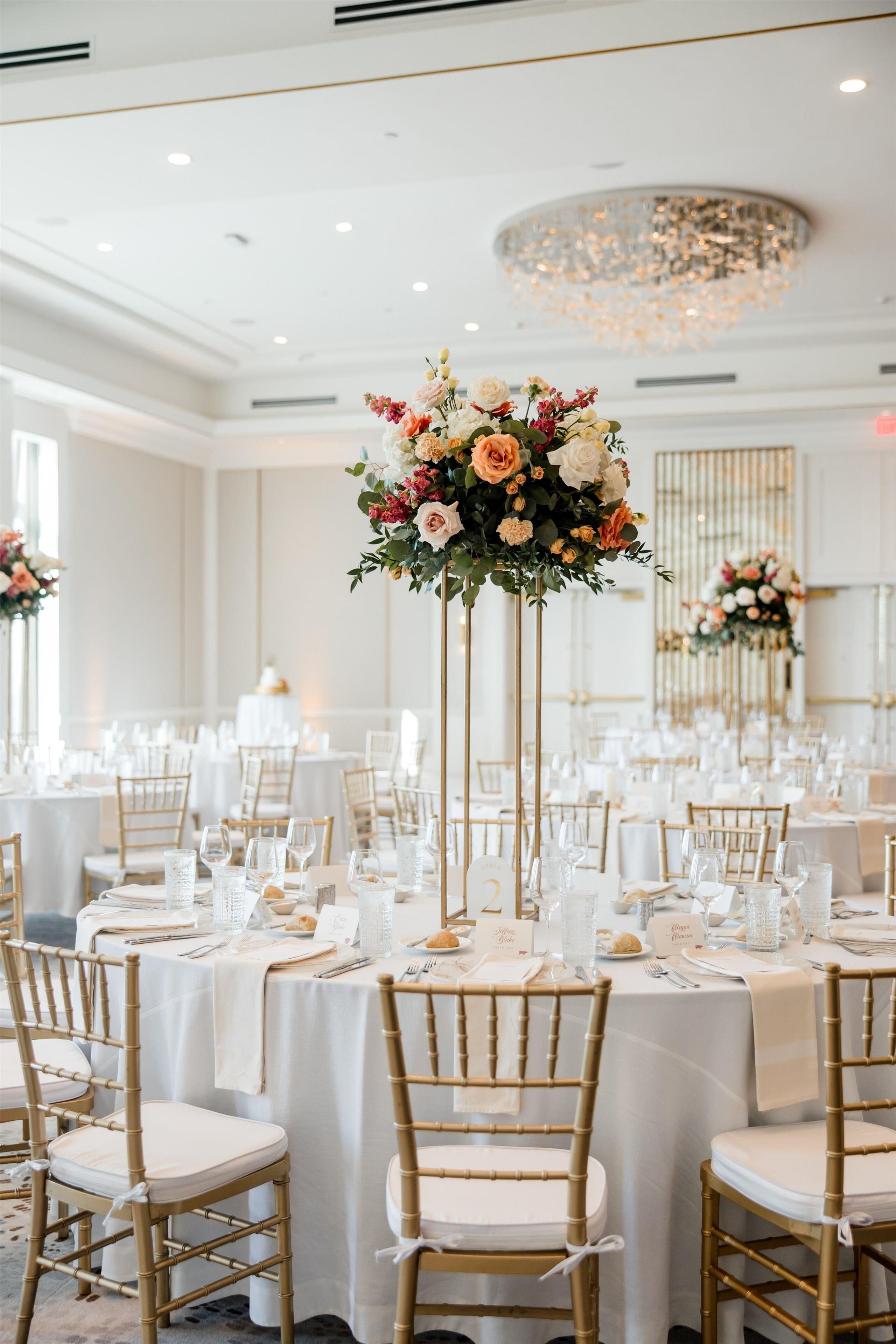 A banquet hall with round tables, gold chairs, and floral centerpieces.