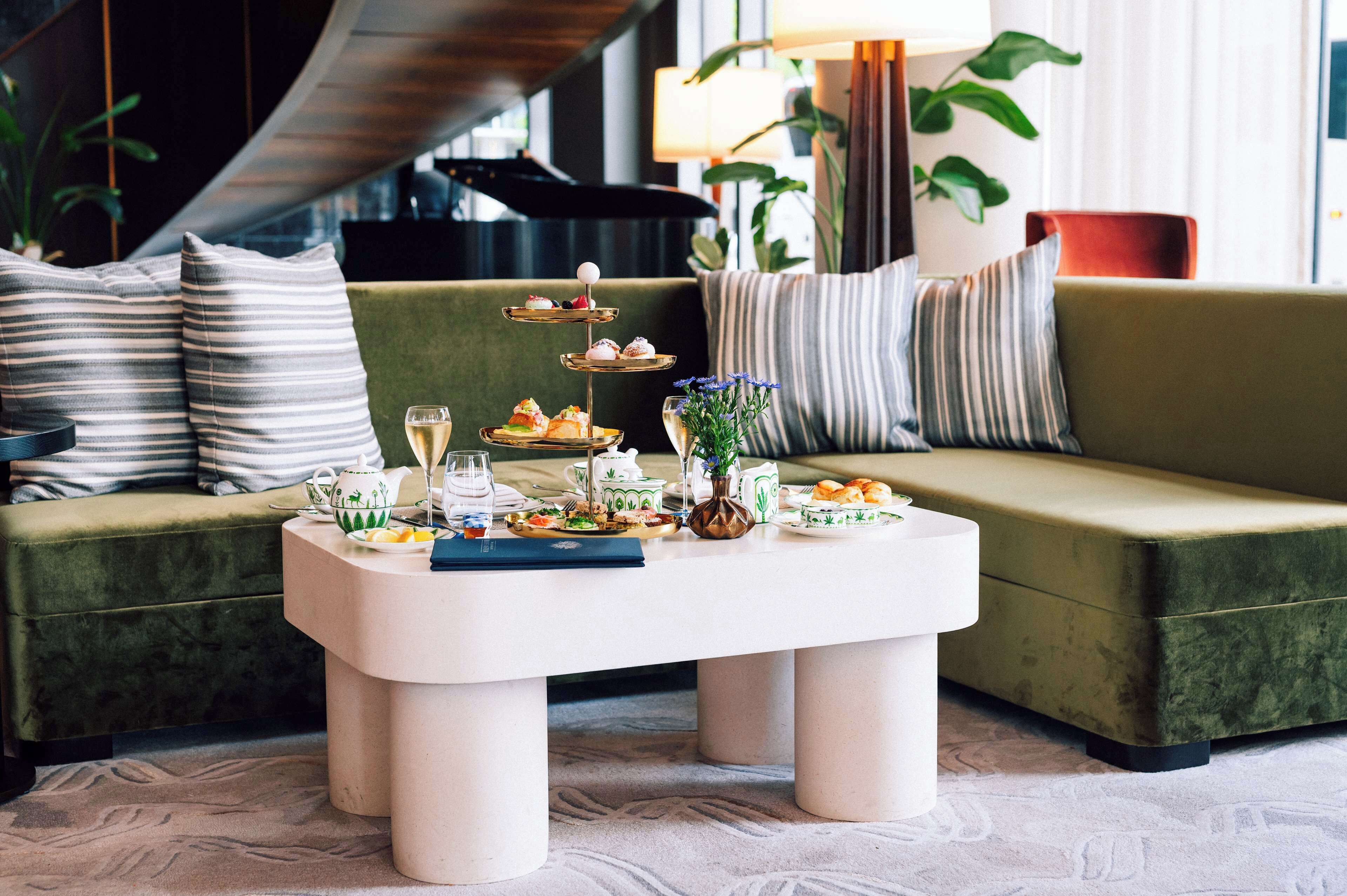 Un comedor con una mesa blanca dispuesta para una comida, un sofá verde con almohadones a rayas y una planta al fondo.