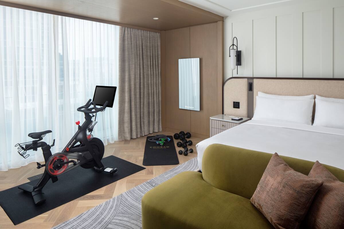 A hotel room with a bed, exercise bike, dumbbells, and a yoga mat.