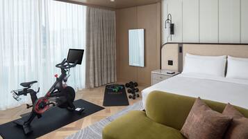 A hotel room with a bed, exercise bike, dumbbells, and a yoga mat.