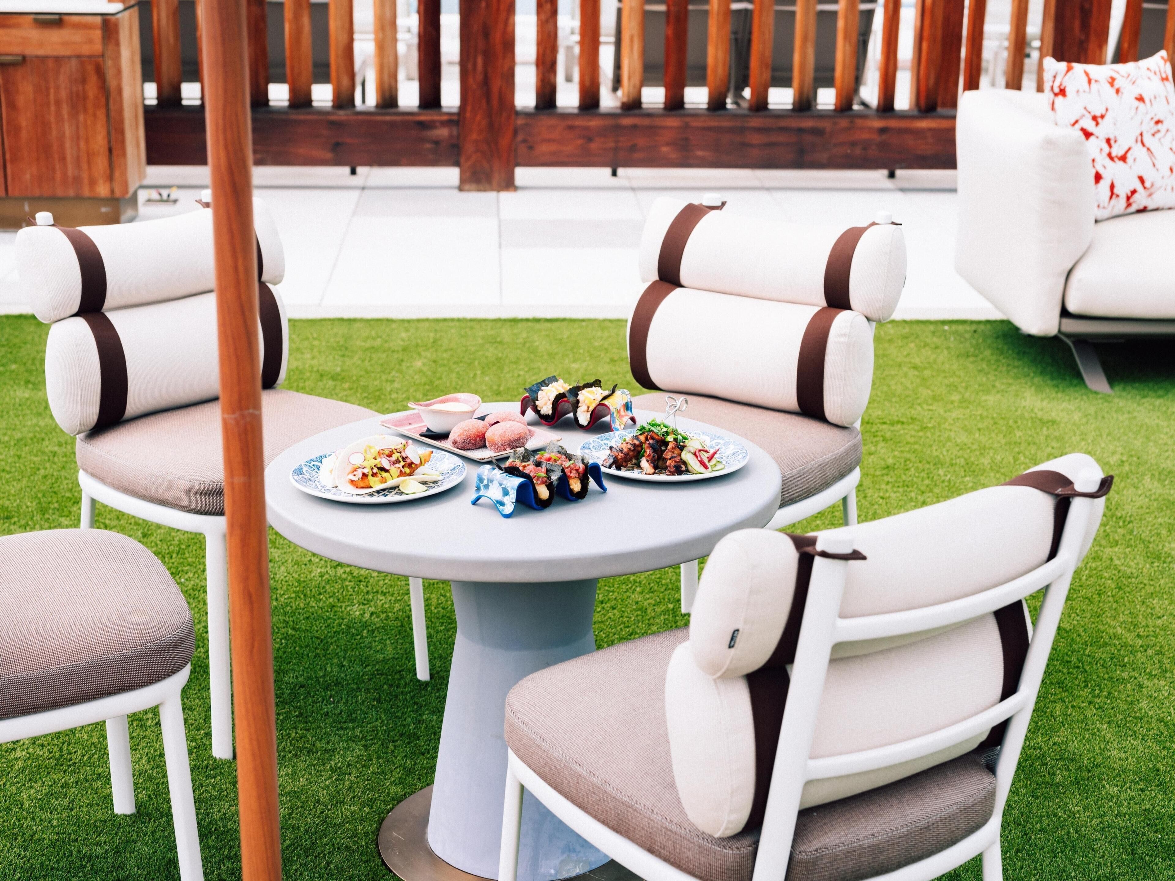 A round table with four chairs, each with a cushion and a brown stripe. The table is surrounded by a wooden fence and a grassy area.
