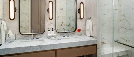 Un baño moderno con dos lavamanos, encimeras de mármol y cabina de ducha de vidrio.