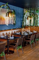 Un restaurante con zona de mesas tipo camarote, mesas con sillas y plantas colgantes.