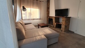 Un salon avec un canapé beige, une petite table en bois, une cheminée en pierre et un téléviseur à écran plat fixé au mur.