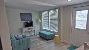 A living room with a television, sofa, bench, and a window with blinds. - Gulf of Mexico Canal Cottage with Boat Dock and Heated Pool (New Port Richey)