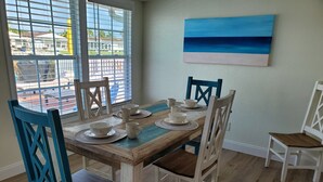 A dining area with a wooden table and blue chairs, a painting on the wall, and a view through the window. - Gulf of Mexico Canal Cottage with Boat Dock and Heated Pool (New Port Richey)