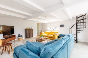 Uma sala de estar moderna com um sofá azul, um sofá amarelo, uma mesa de centro de madeira e uma televisão.
