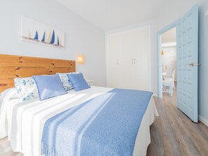 Quarto com cabeceira de madeira, cama com colcha azul e branca e pintura de veleiros na parede.