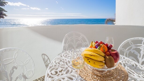 Taula amb fruita i un got de vi a un balcó amb vista al mar.