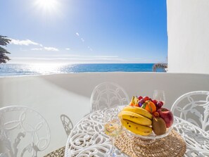 Uma mesa com frutas e um copo de vinho numa varanda com vista para o mar.
