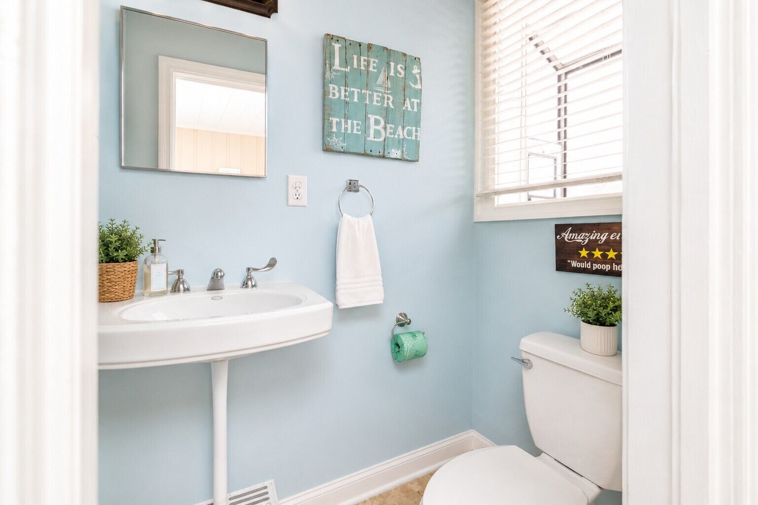 A bathroom with a sink, mirror, toilet, and a window with blinds.