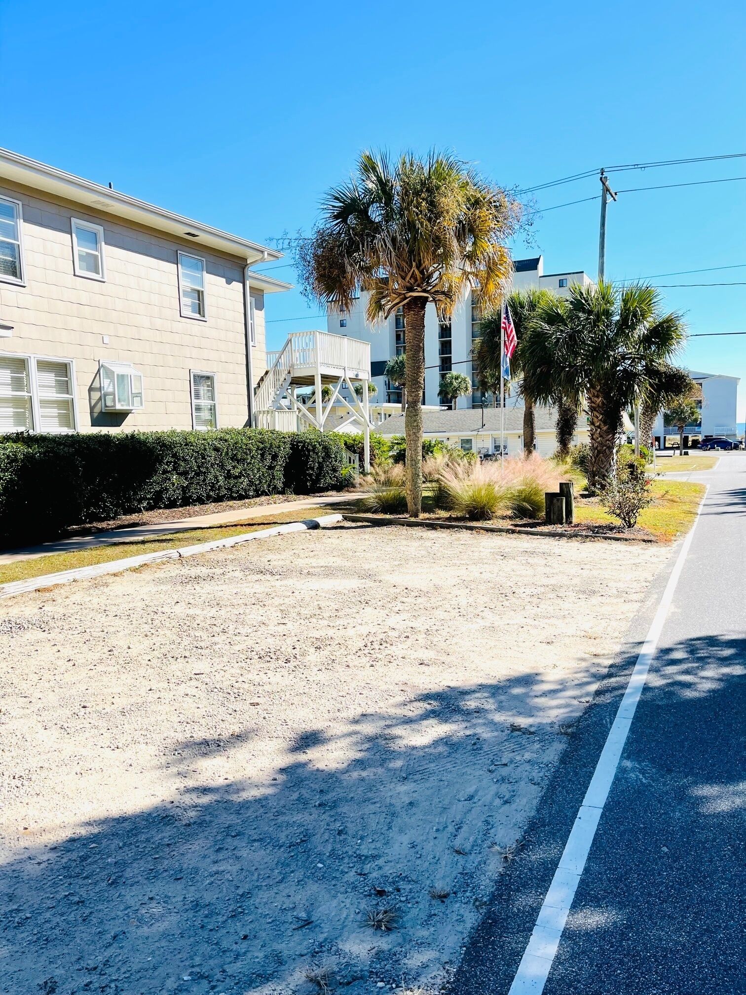 A residential area with a sandy lot, a road with a white line, and a building with a balcony.