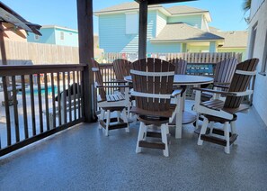 A covered outdoor seating area with Adirondack chairs and a small round table, overlooking a swimming pool.