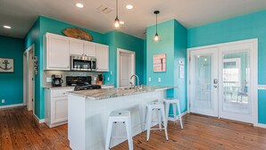 A kitchen with white cabinets, a central island with stools, a microwave, and a coffee maker. - Bring your Big Group, 12 BR/8 BA, Private Pool, Walk to the Beach! (Port Aransas)