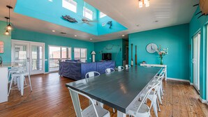 A spacious room with a long dining table, white chairs, a blue accent wall, and a ceiling fan. - Bring your Big Group, 12 BR/8 BA, Private Pool, Walk to the Beach! (Port Aransas)