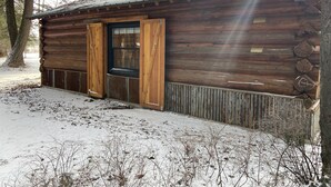 Een rustieke blokhut met een houten deur en raam, omgeven door sneeuw en bomen.