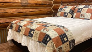 Een slaapkamer in blokhutstijl met een houten vloer, een geborduurde bedsprei en twee kussens met een bergleeuw dessin.