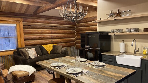 Een rustiek houten interieur met een eettafel voor vier personen, een zwarte koelkast, een keukenkraan en een kroonluchter.