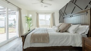 Un dormitorio con cama, ventilador de techo, ventana y una planta.