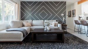 Una sala moderna con un sofá modular, una mesa de centro de madera oscura y una pared con estampado geométrico.