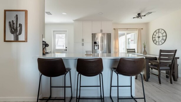 Una cocina moderna con armarios blancos, una isla central con taburetes y un refrigerador, además de un reloj en la pared.