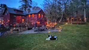 Una casa rústica de color rojo con un césped cuidado y un perro descansando en el pasto.