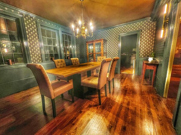 Un comedor con una mesa de madera y seis sillas, una araña y un papel tapiz estampado.