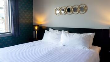 A neatly made bed with white linens, a wall-mounted circular mirror, and a bedside lamp.