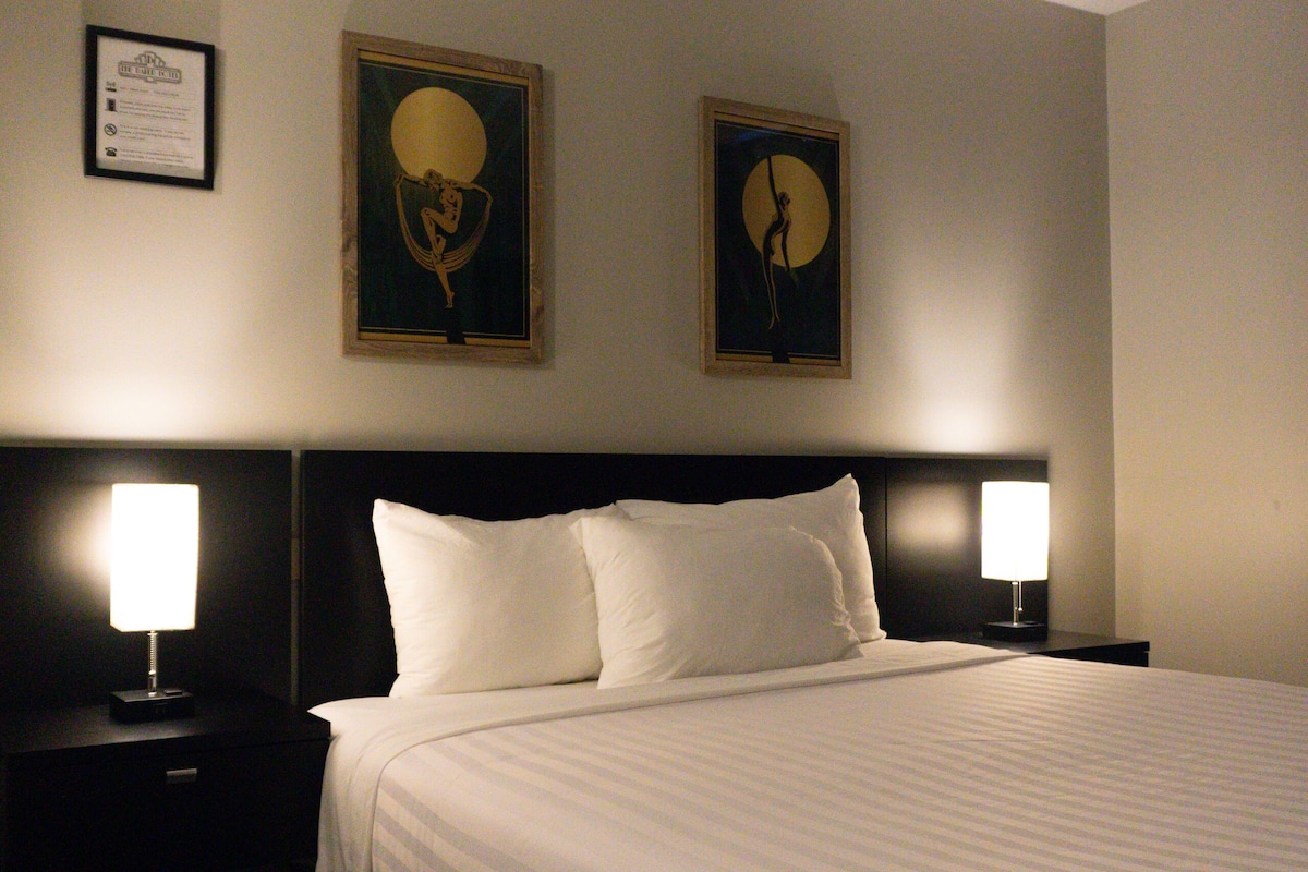 A hotel room with a large bed, two bedside lamps, and two framed artworks on the wall.