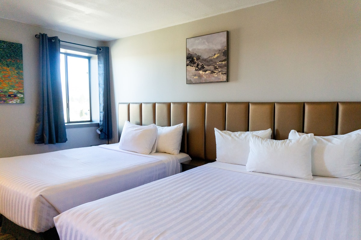 A hotel room with two beds, a window with curtains, and a painting on the wall.