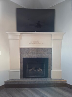 A fireplace with a TV mounted above it, a stone hearth, and a dark wood floor. - The Baker Hotel (Cranbrook)