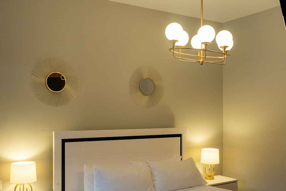 A neatly made bed with white linens, two bedside tables with lamps, and a modern ceiling light fixture.