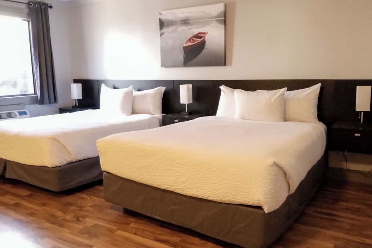 A hotel room with two beds, wooden flooring, a painting on the wall, and a window with curtains.