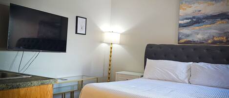 A hotel room with a bed, a TV, a desk, and a painting on the wall.
