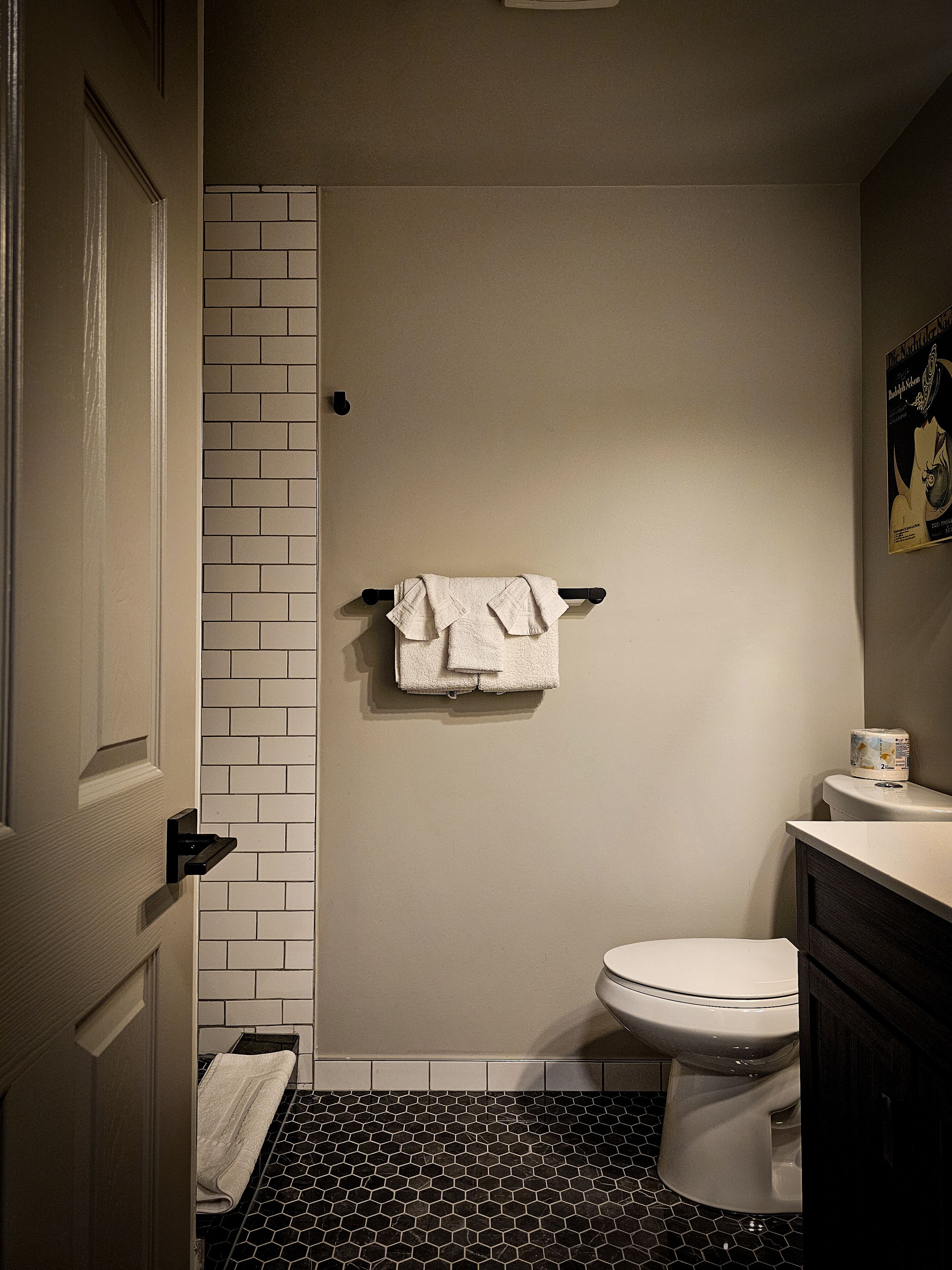 Un baño con un inodoro blanco, un perchero con una toalla doblada, un dispensador de papel higiénico y un suelo de baldosas blanco y negro.