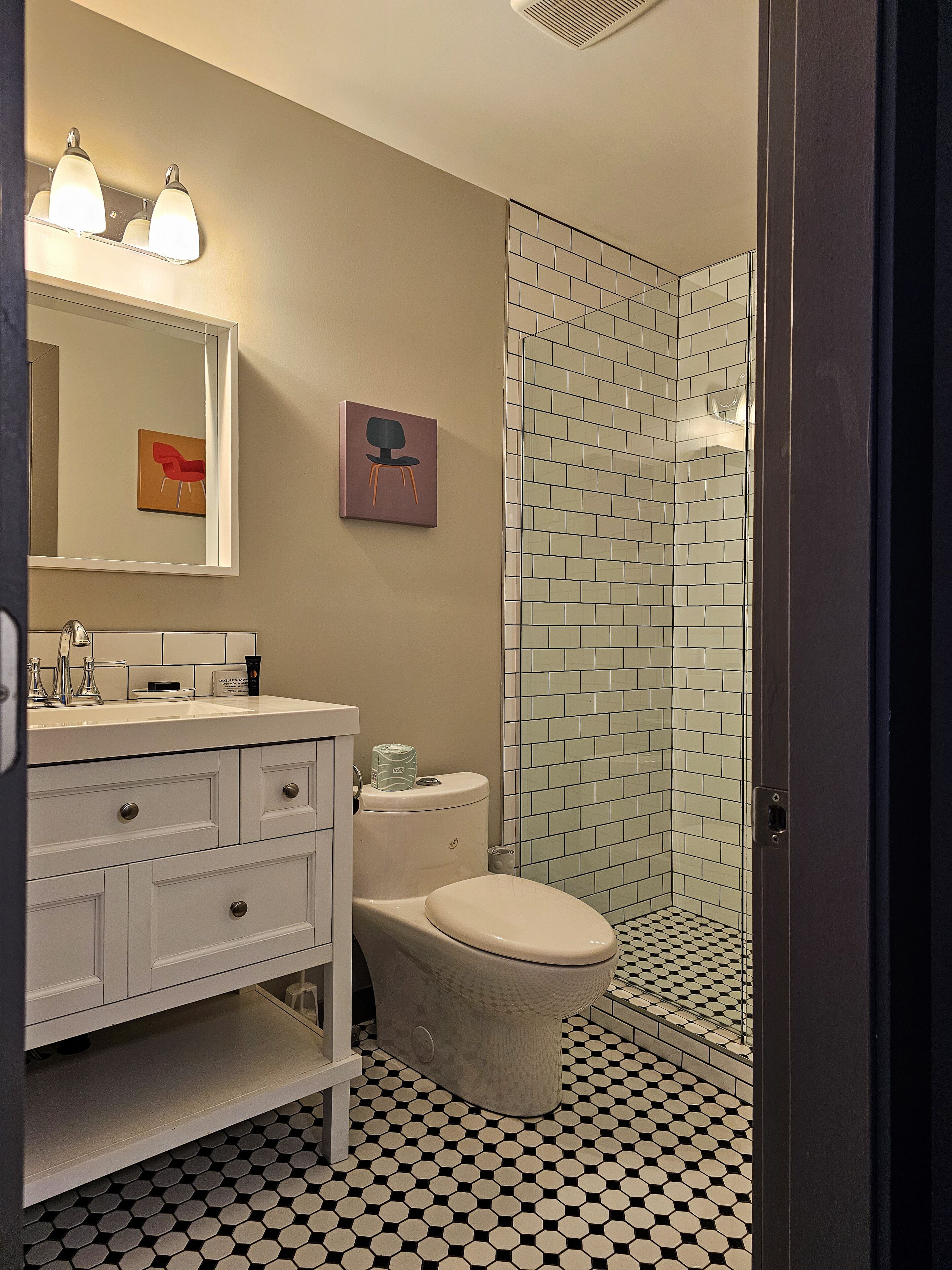 A bathroom with a white sink, mirror, and toilet, a shower with a glass door, and a tiled floor.