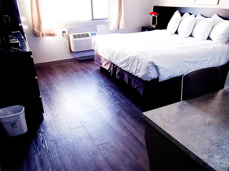 Ett hotellrum med en säng, ett skrivbord, en stol, en värmare och ett fönster med gardiner.