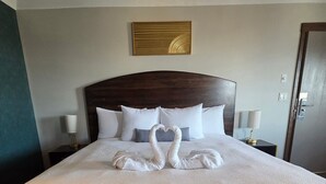 A hotel room with a large bed, two bedside lamps, a wooden headboard, and a decorative wall piece. - The Baker Hotel (Cranbrook)