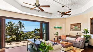 A spacious living room with a balcony overlooking palm trees and the ocean. - Kauai Luxury home, Private Pool & Spa, walk to the beach, restaurants and shops (Koloa)